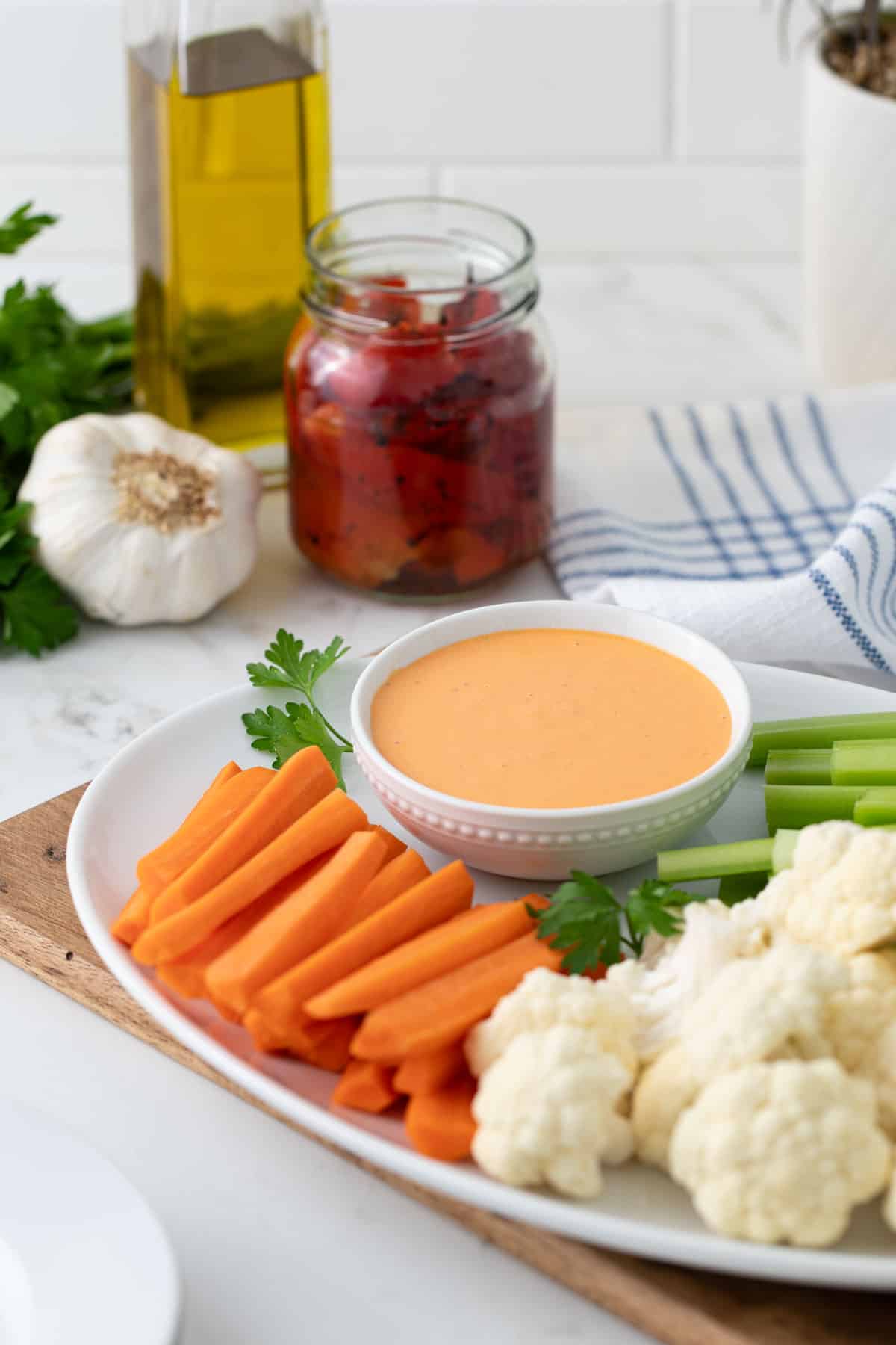 A small bowl of red pepper aioli on a platter with carrots, celery, and cauliflower.