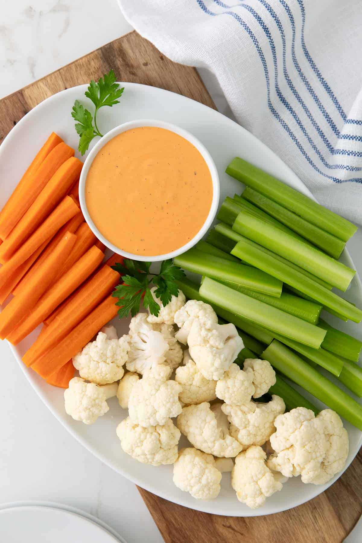 Overhead view of a small bowl of red pepper aioli on an oval white platter with vegetables.