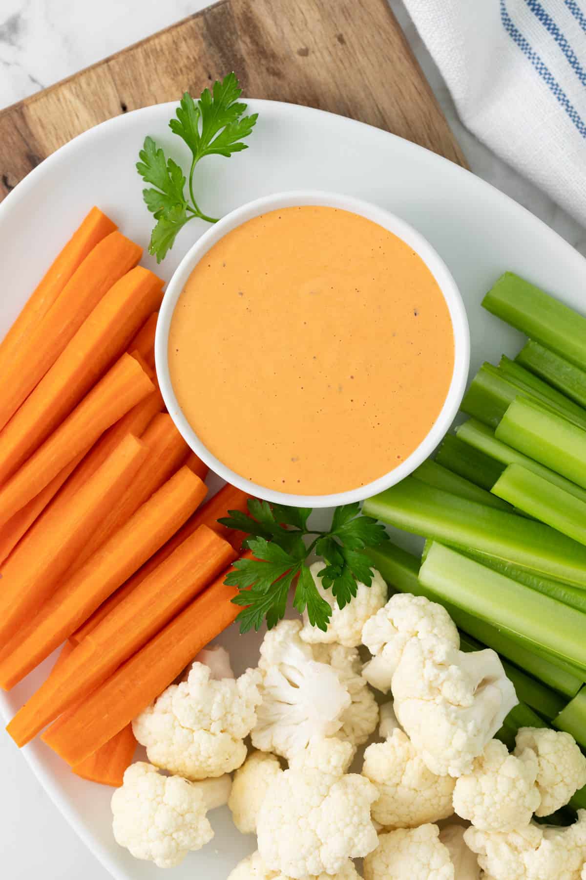 Overhead close up view of a small white bowl of red pepper aioli on a platter with vegetables.