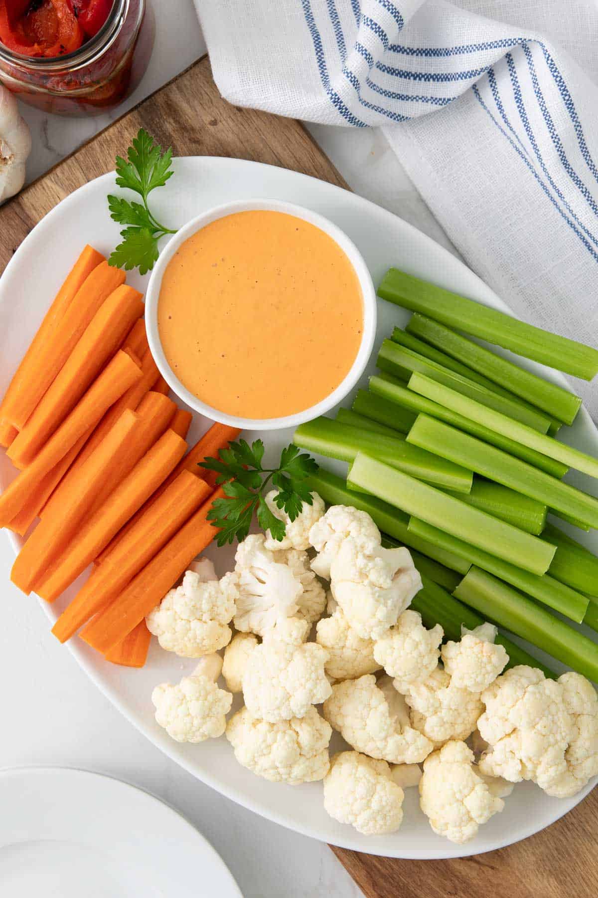 Overhead view of a bowl of red pepper aioli on a platter with veggies.
