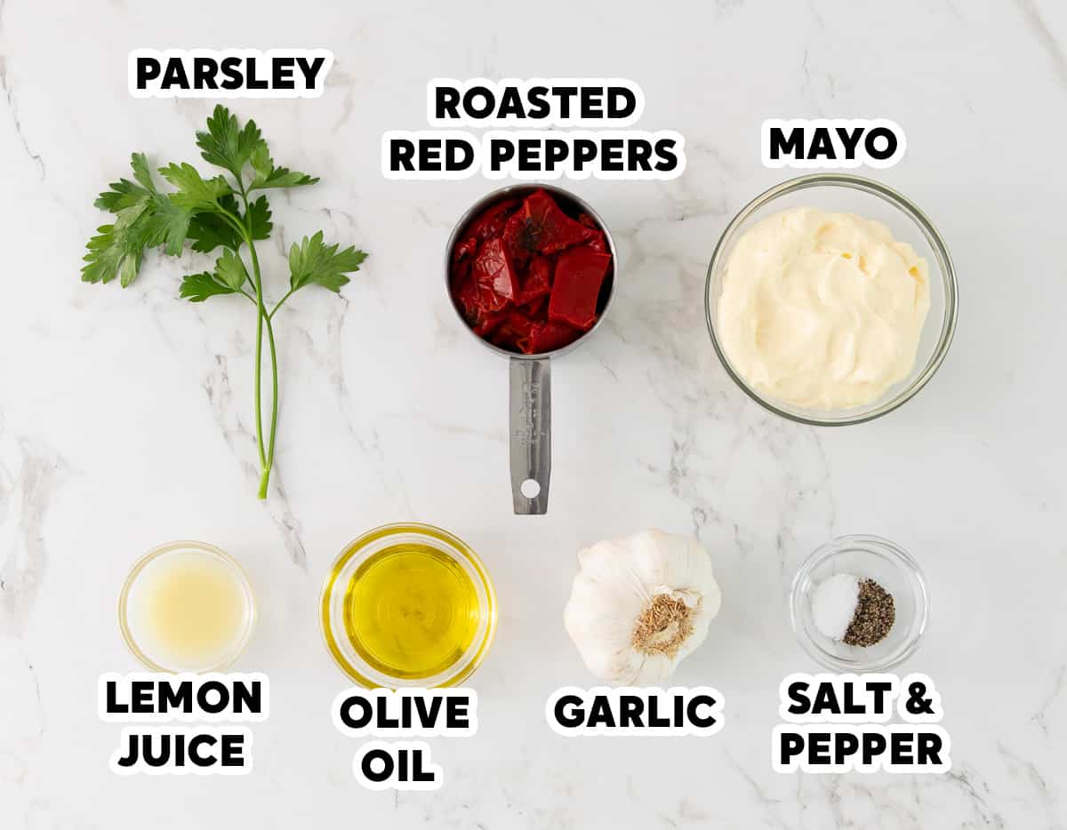Overhead view of ingredients for making red pepper aioli on a white marble surface with overlay text.