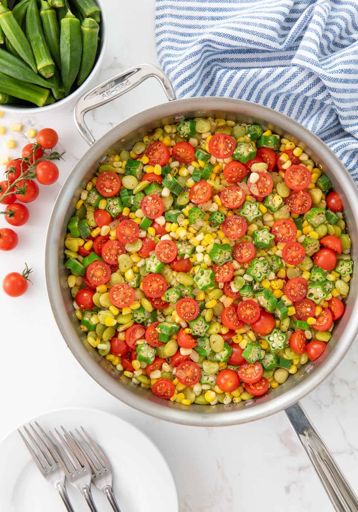 Overhead view of summer succotash in a saute pan by a blue striped kitchen towel.