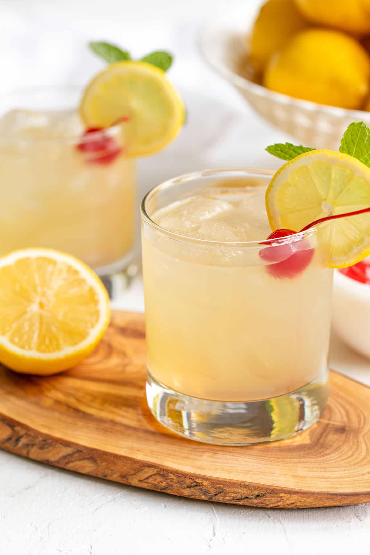 Front view of a garnished bourbon lemonade cocktail with a bowl of lemons in the background.