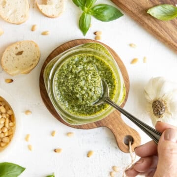 Overhead view of a spoon being dipped into a jar of homemade basil pesto.
