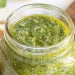 Closeup view of a jar of basil pesto. Overlay text is at the top of the image.