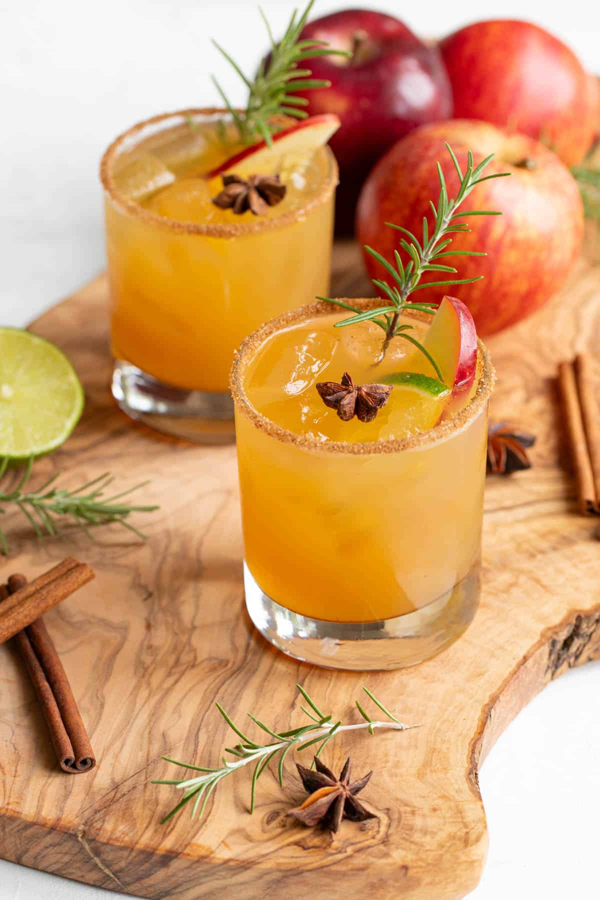 Front angled view of two garnished apple cider margaritas on a wood surface.
