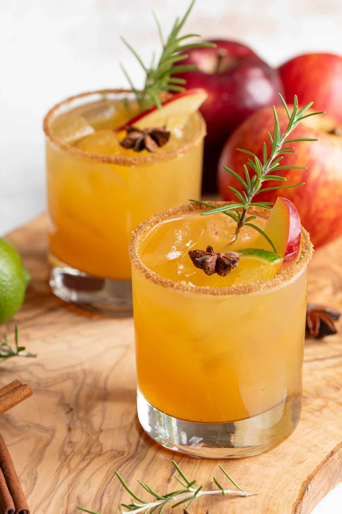Front view of two garnished apple cider margaritas on a wood surface.