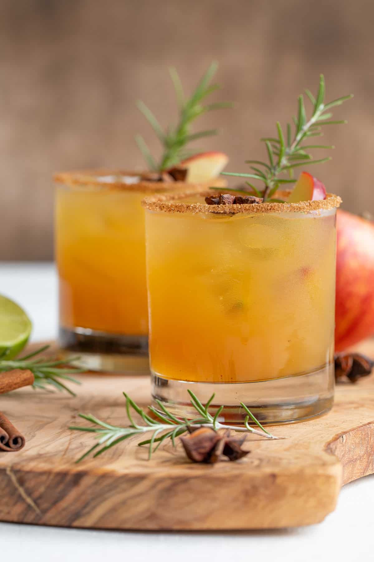 Front view of two garnished apple cider margaritas on a wood surface.