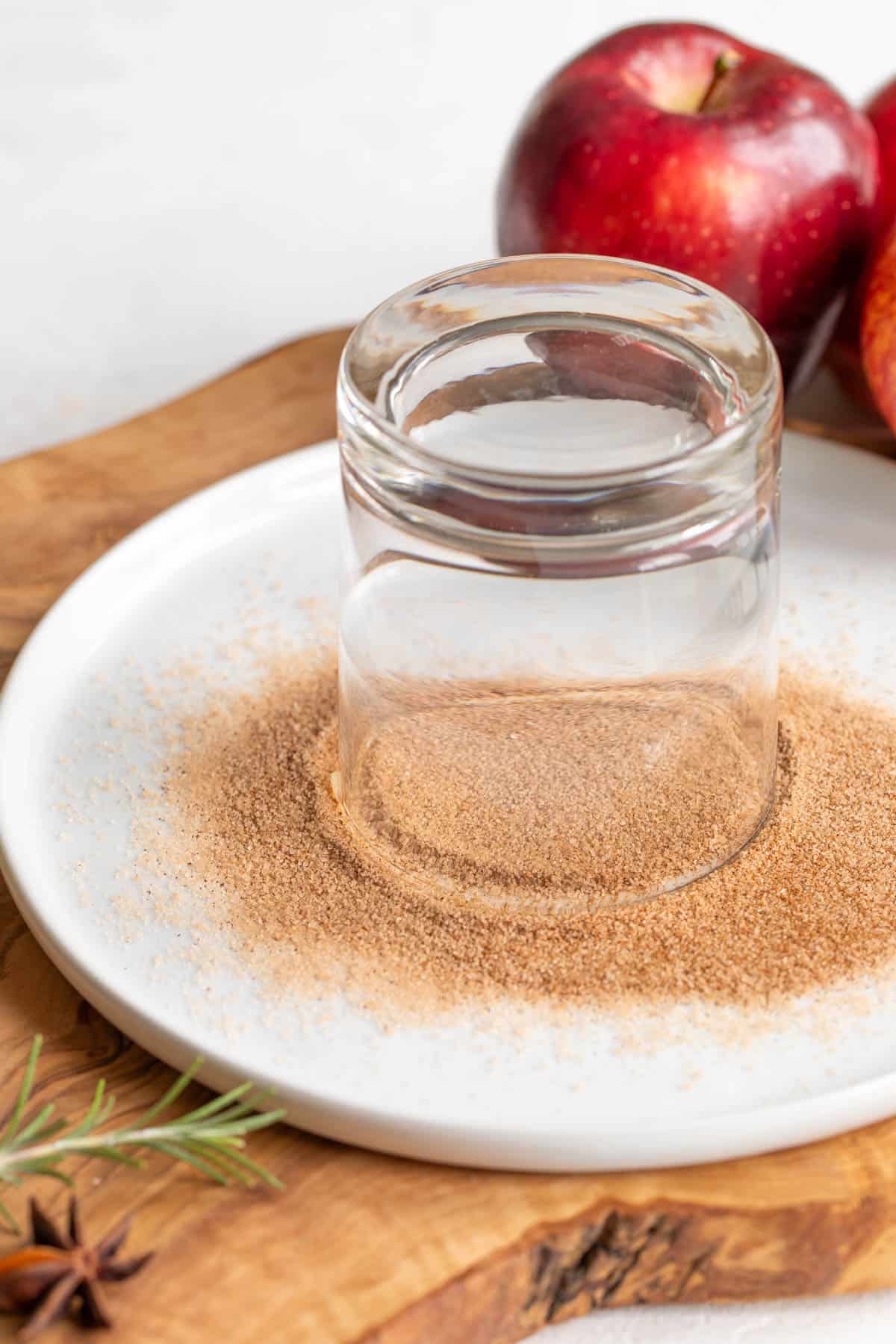 A glass is dipped into a mixture of ground cinnamon and sugar on a plate to make an apple cider margarita.