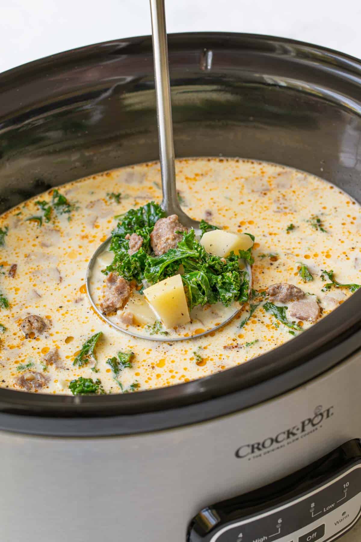 A stainless ladle ladling Zuppa Toscana soup from a Crock Pot.