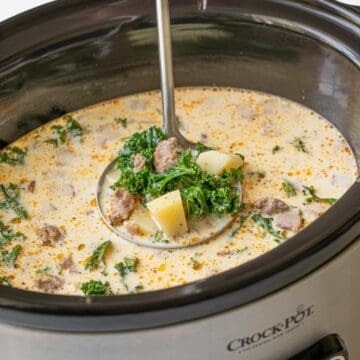 Close-up view of a stainless ladle in a crock pot of Zuppa Toscana soup.