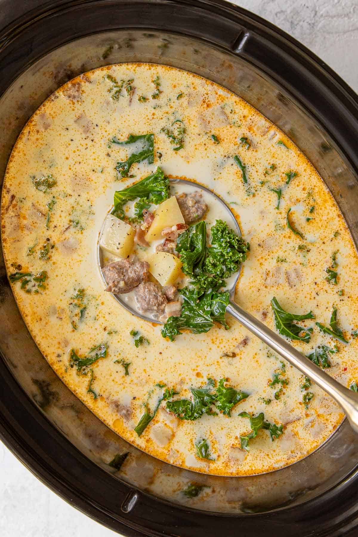 Overhead view of a ladle in Zuppa Toscana soup in an oval crockpot.