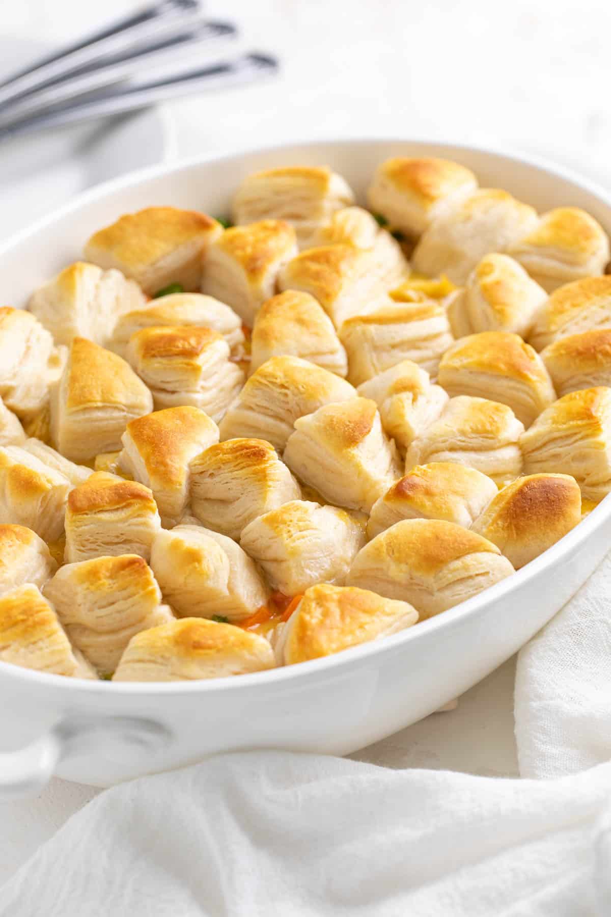 Cheesy chicken pot pie topped with quartered canned biscuits in an oval white baking dish.