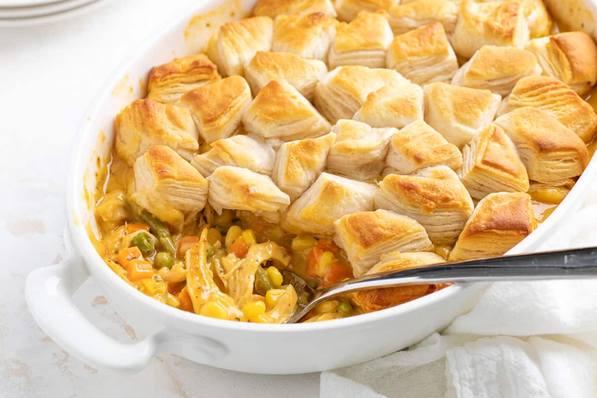 Closeup view of a serving spoon in a dish of cheesy chicken pot pie topped with canned biscuits.