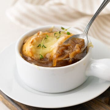 Close up view of a spoon in a white bowl of French onion soup.
