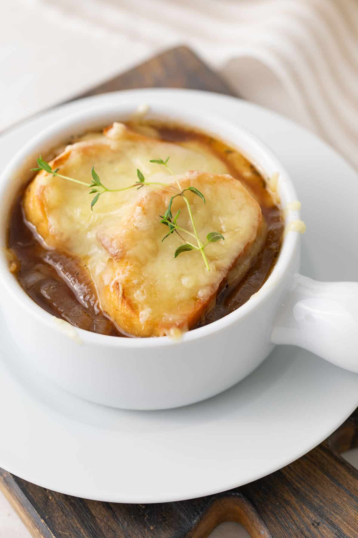 Angled view of a bowl of French onion soup garnished with a sprig of fresh thyme.