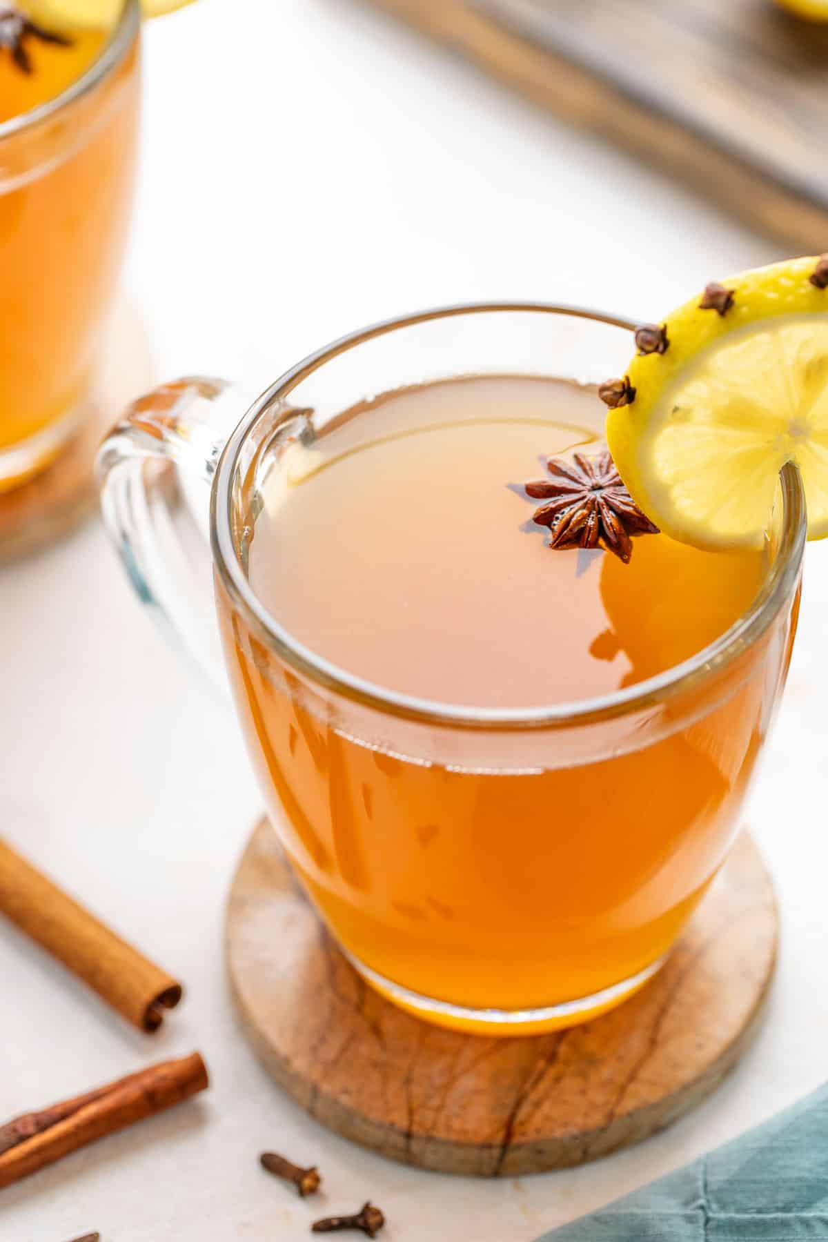 Angled view of a hot toddy drink in a clear glass mug garnished with a clove-studded lemon slice and star anise.