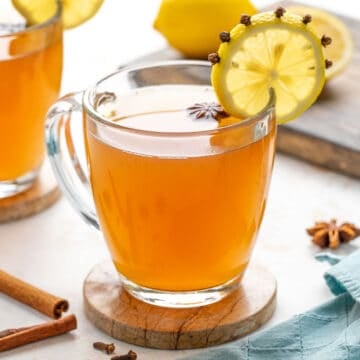 Front view of a garnished hot toddy drink in a clear glass mug.