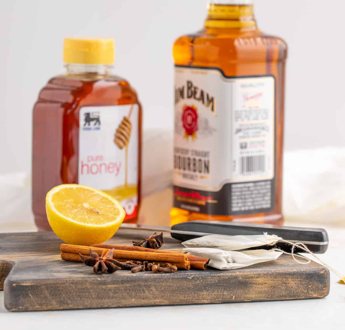 Front view of ingredients for making a hot toddy: Whiskey, honey, tea bags, a lemon, cinnamon sticks, and star anise.