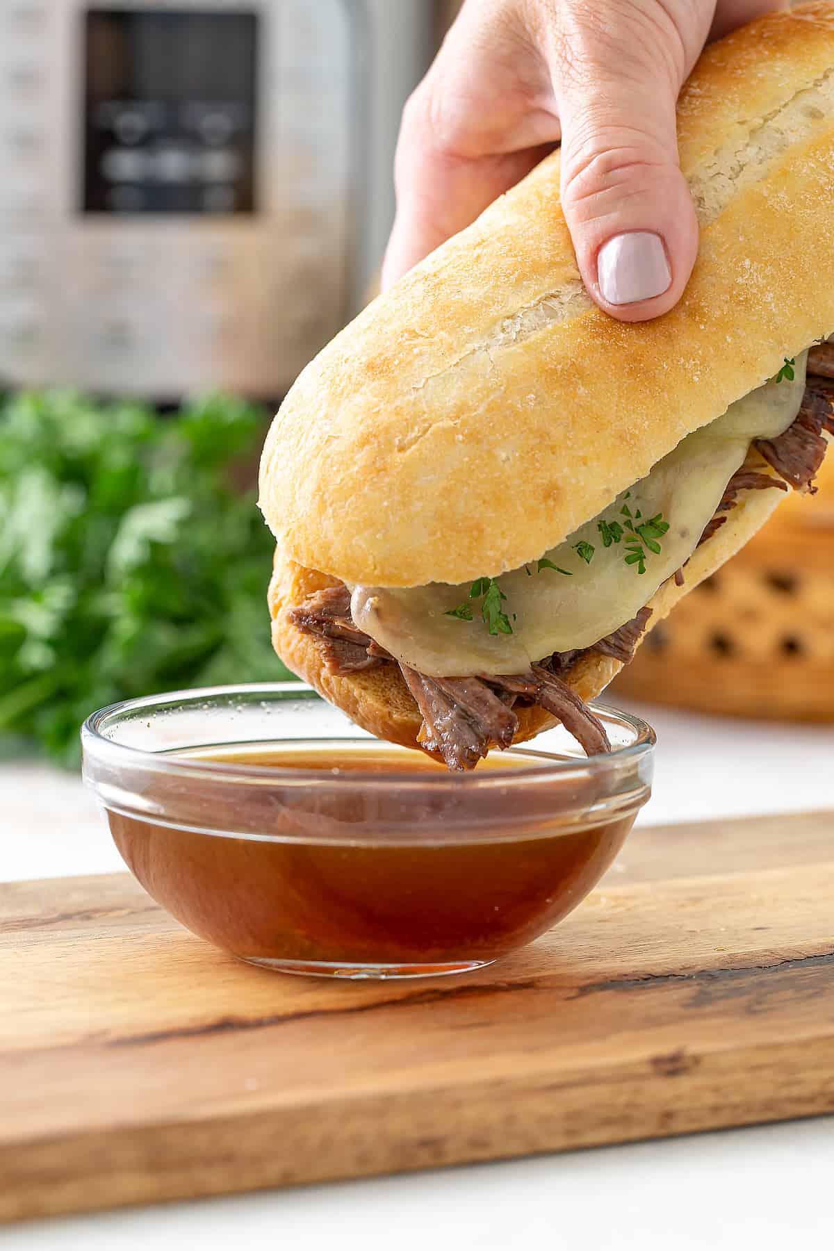 A French dip sandwich being dipped into a bowl of au jus. An Instant Pot is in the background.