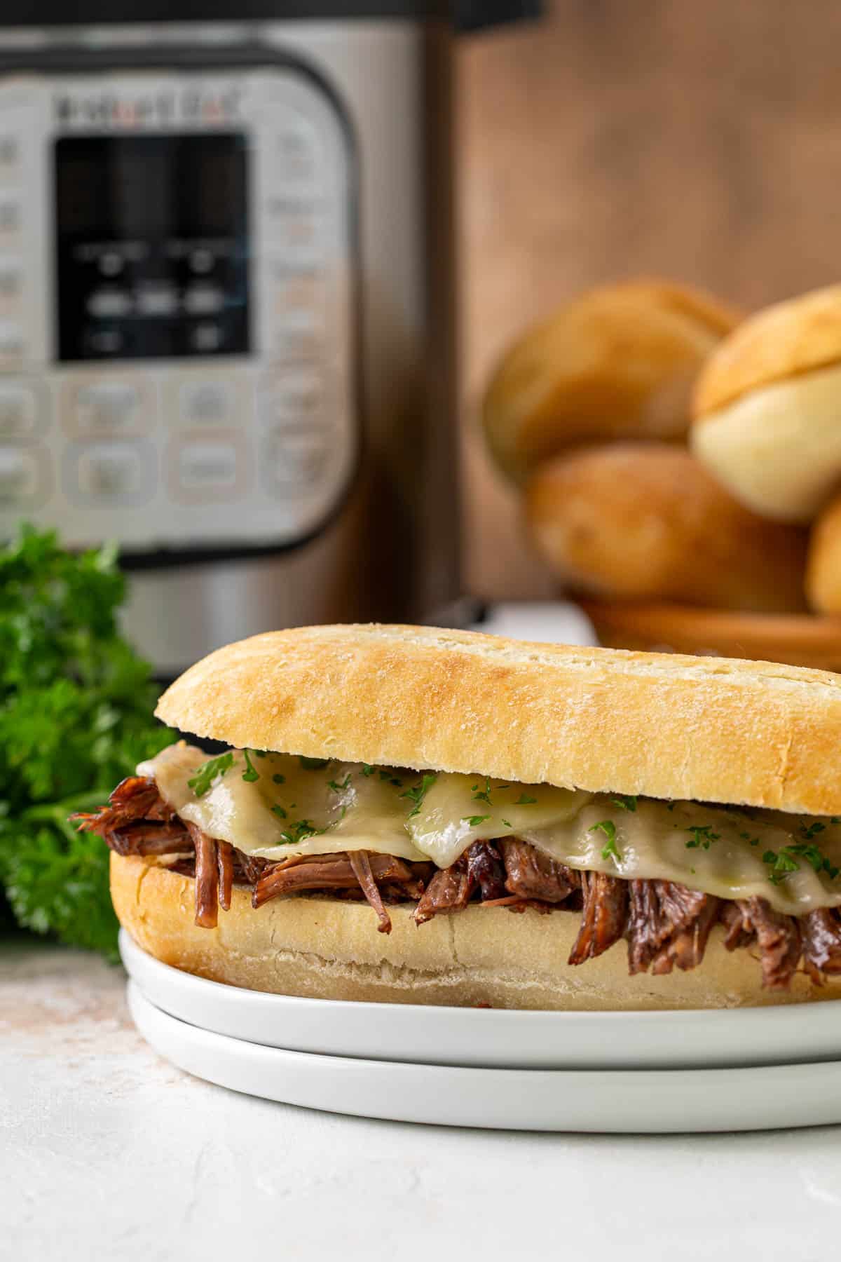 Front view of a French Dip sandwich on a white plate. An instant pot pressure cooker is in the background.