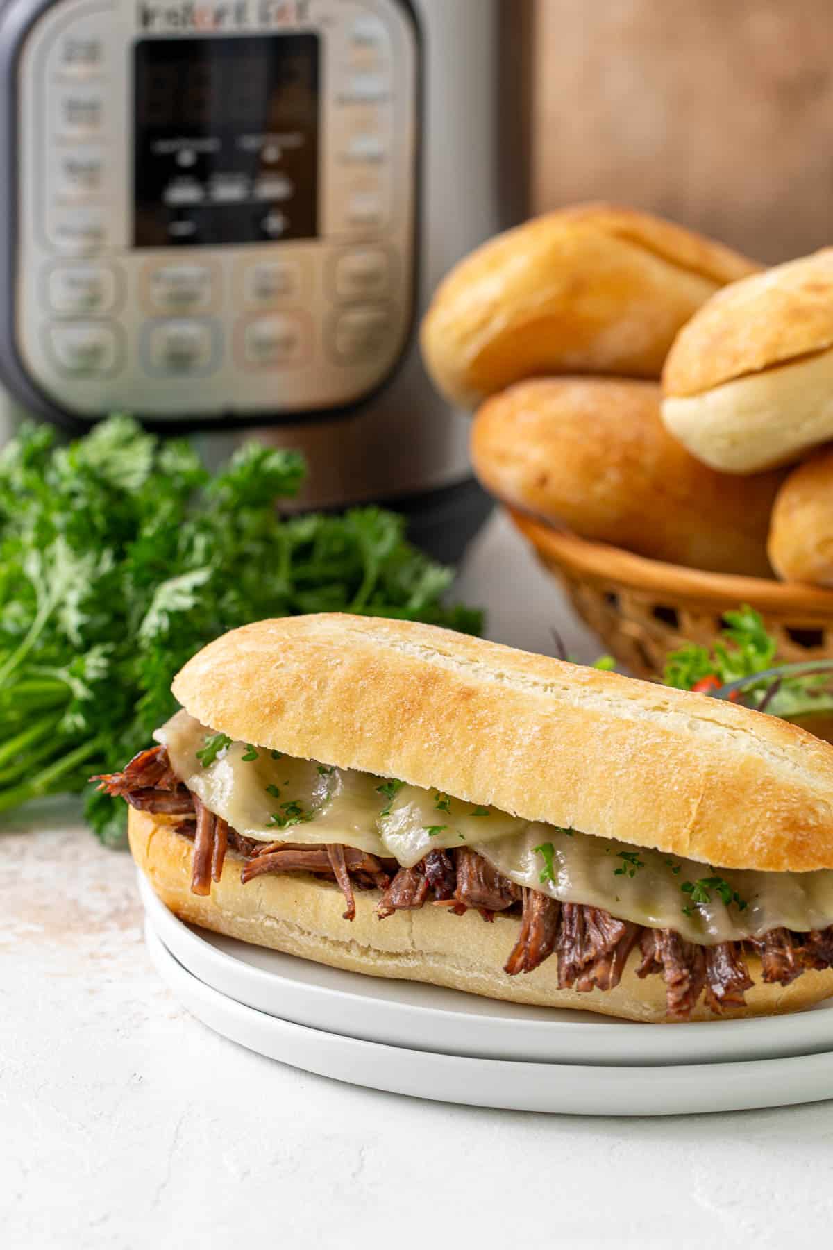 Front view of a French dip sandwich on a white plate. An instant pot is in the background.