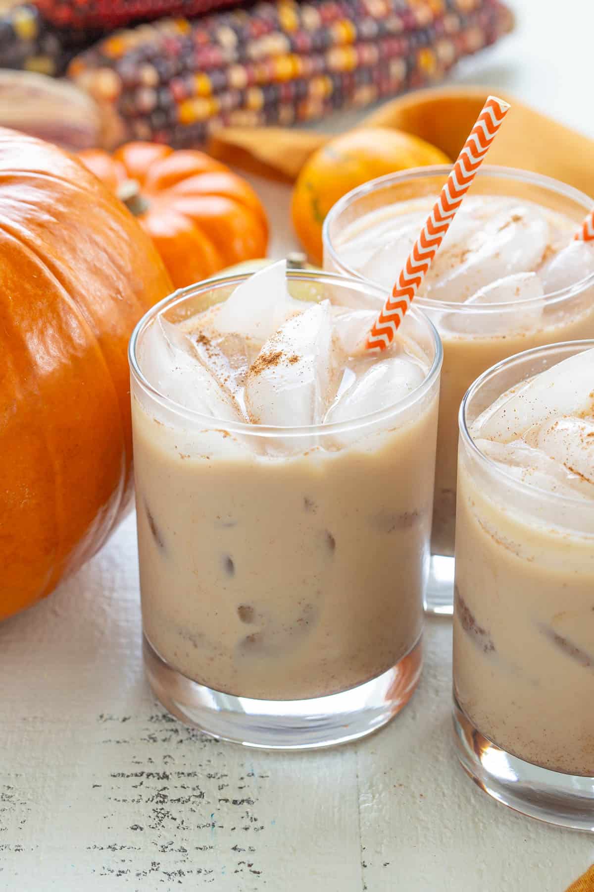 Front view of three pumpkin spice white Russians in glasses with and orange and white paper straw.