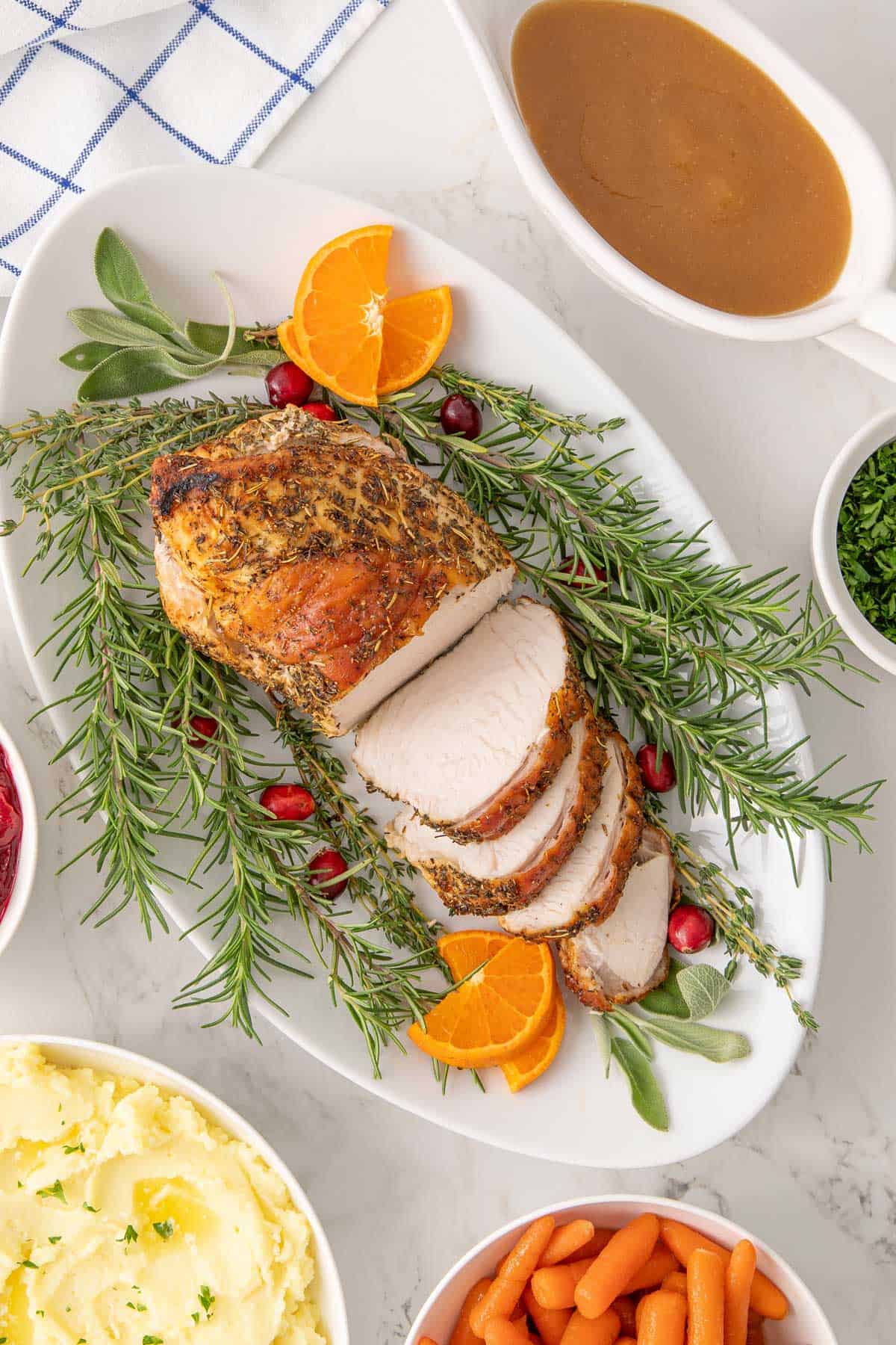 Overhead view of a partially sliced turkey breast on a platter beside bowls of side dishes and gravy.