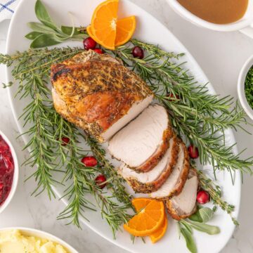 Overhead view of a partially sliced boneless turkey breast on a platter with garnishes.