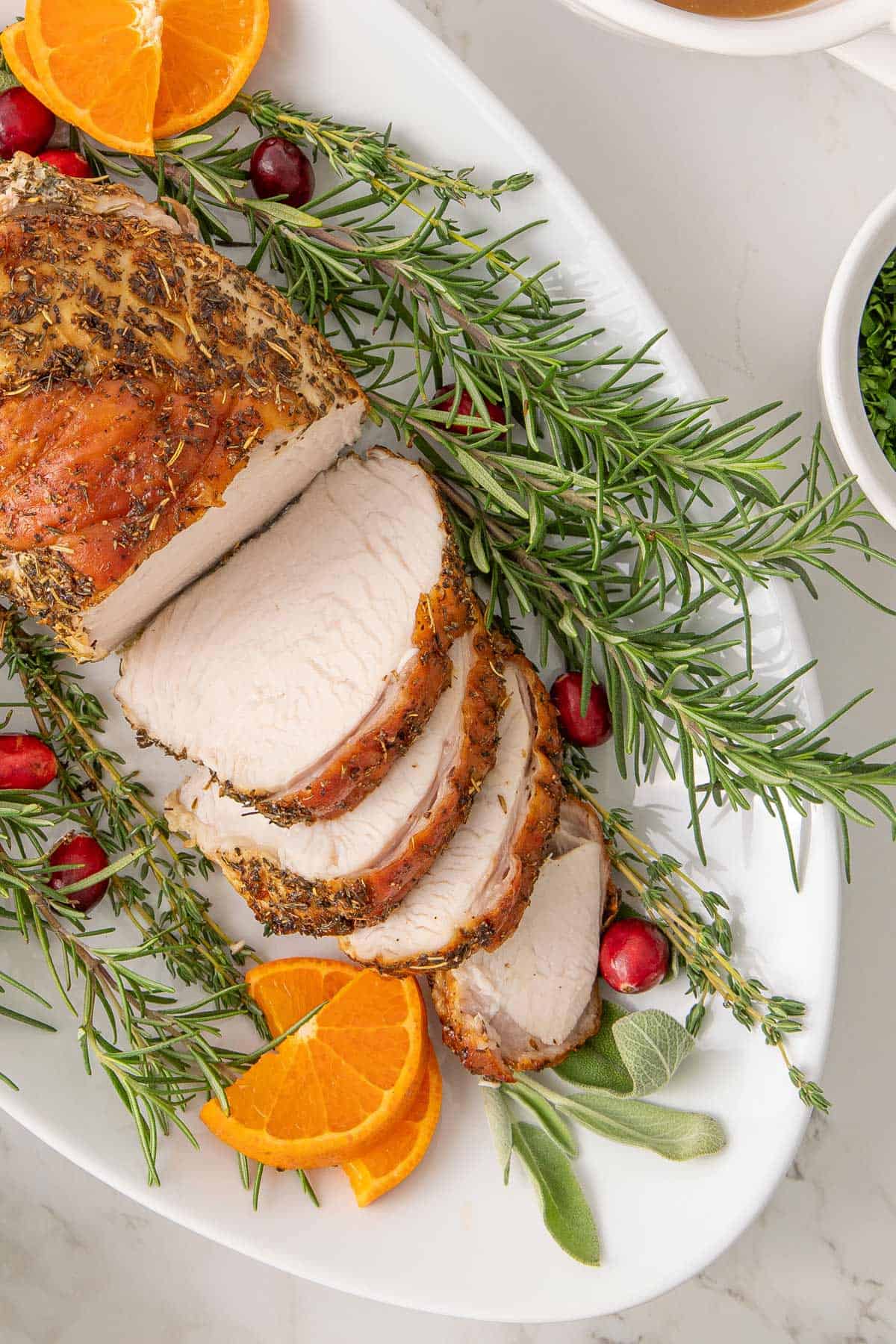 Overhead close up view of a partially sliced boneless turkey breast on an oval white platter.