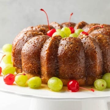 Front view of a Bacardi rum cake garnished with cherries and grapes on a white cake stand.