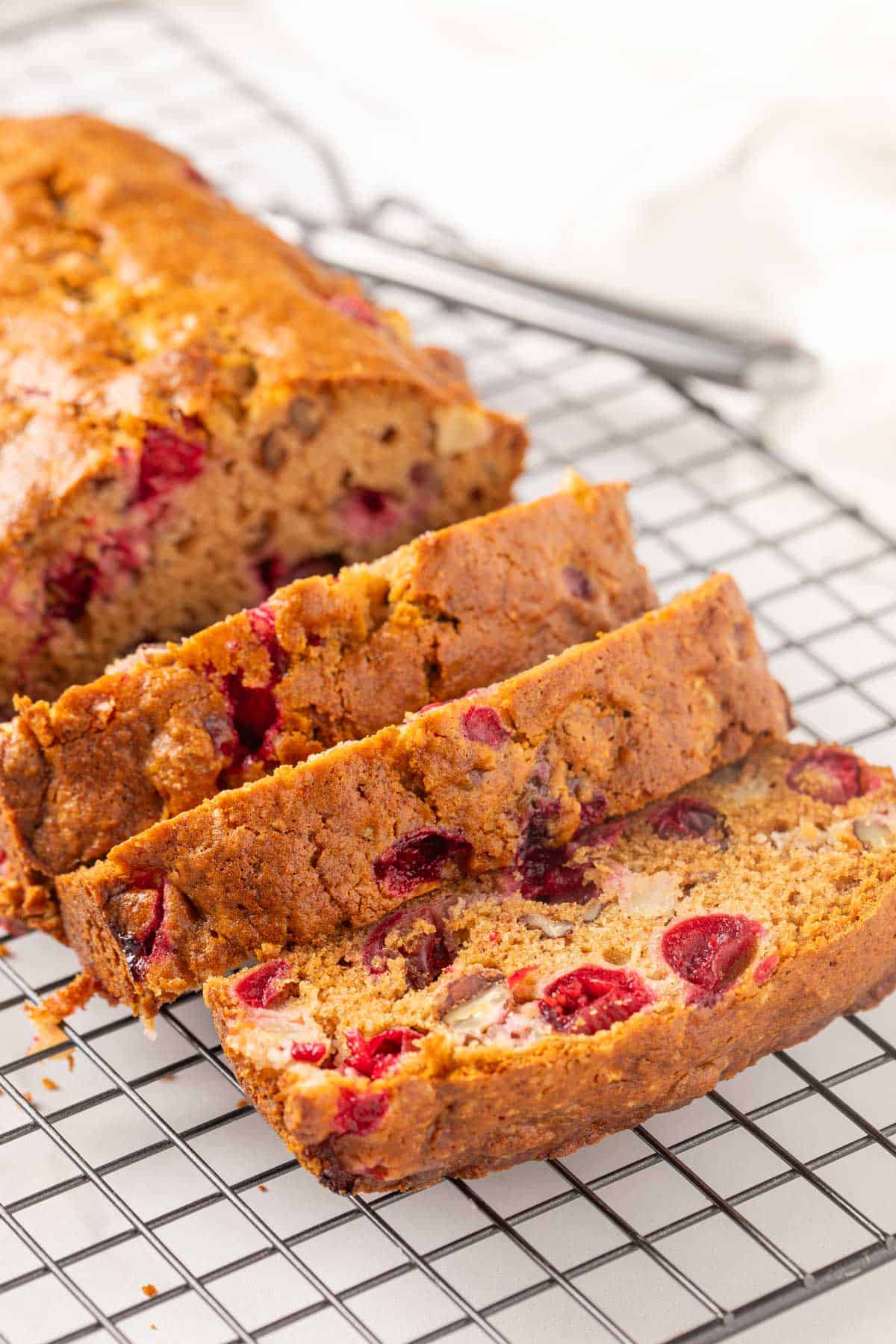 Front view of a partially sliced loaf of cranberry apple bread on a black wire rack.