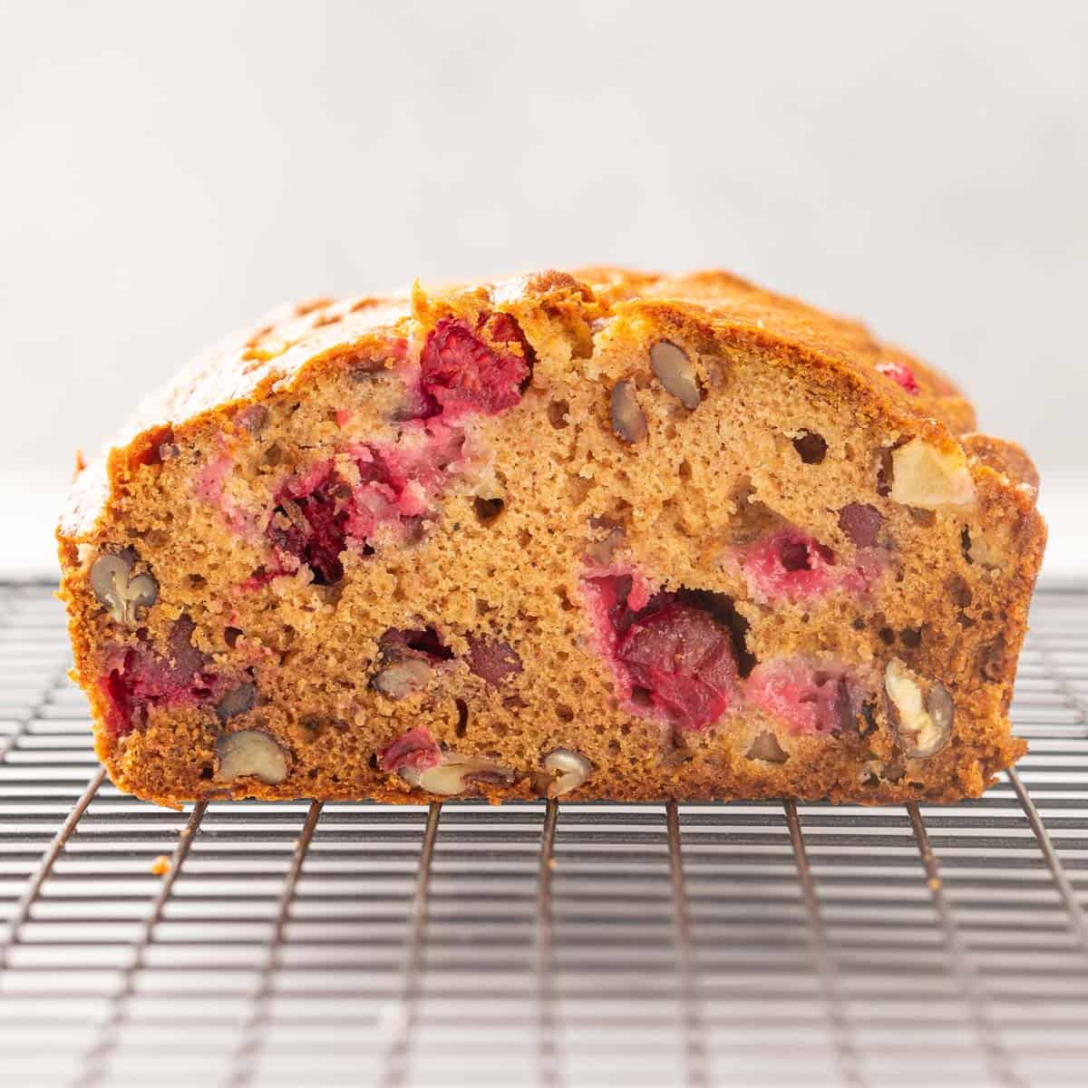 Front close up view of a sliced loaf of cranberry apple bread on a wire rack.
