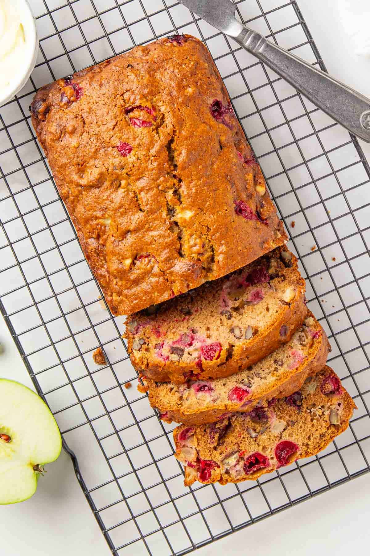 Overhead view of a partially sliced loaf of cranberry apple bread on a wire rack.