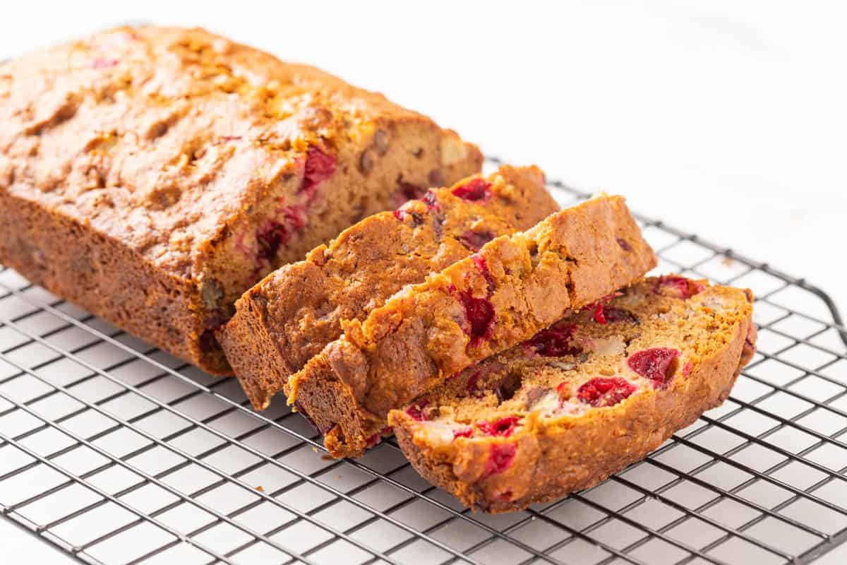 A partially sliced loaf of apple cranberry bread on a wire rack.