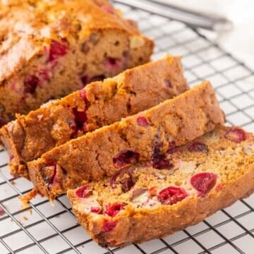 Close up view of a partially sliced loaf of cranberry apple bread on a wire cooling rack.