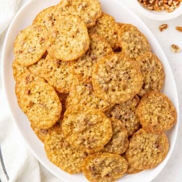Overhead view of oatmeal lace cookies on an oval white platter.