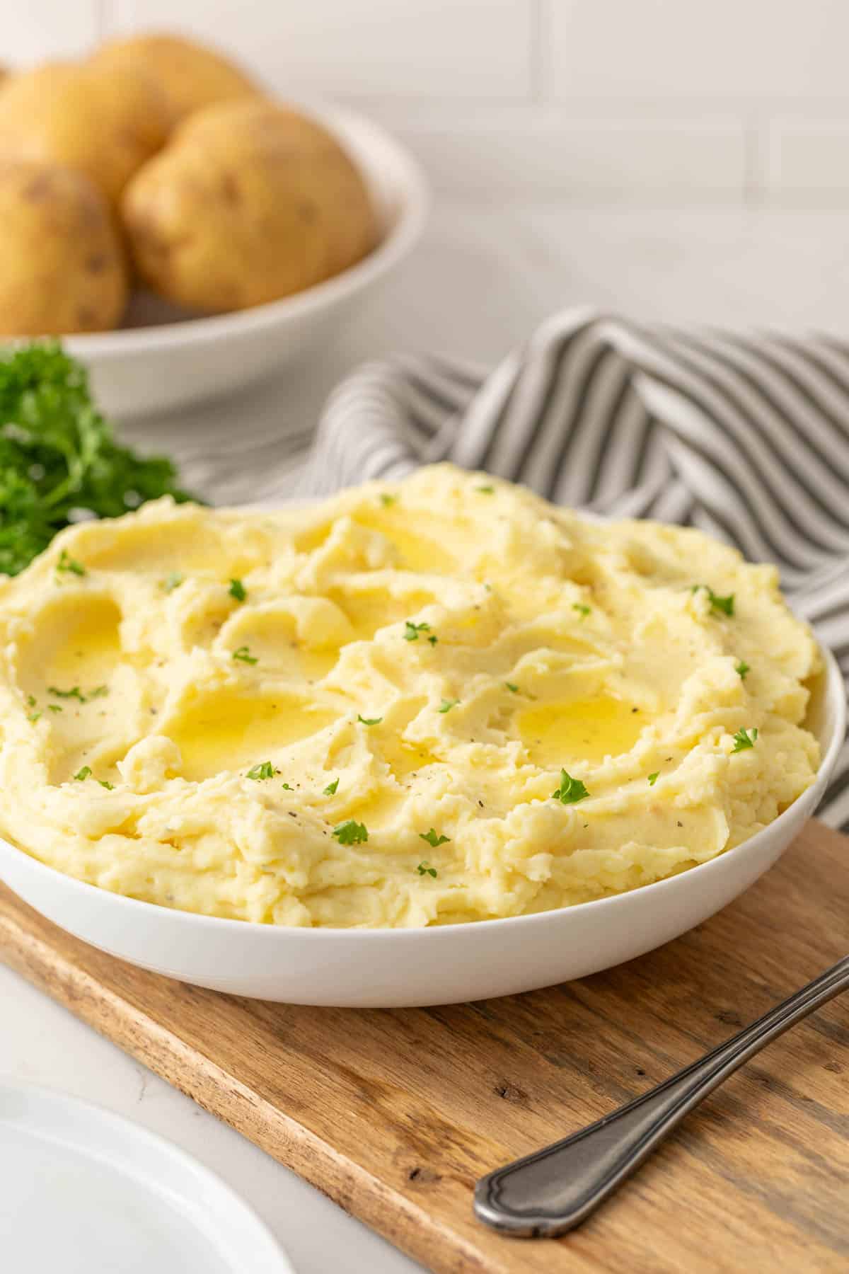 Front view of a bowl of mashed potatoes garnished with chopped parsley.