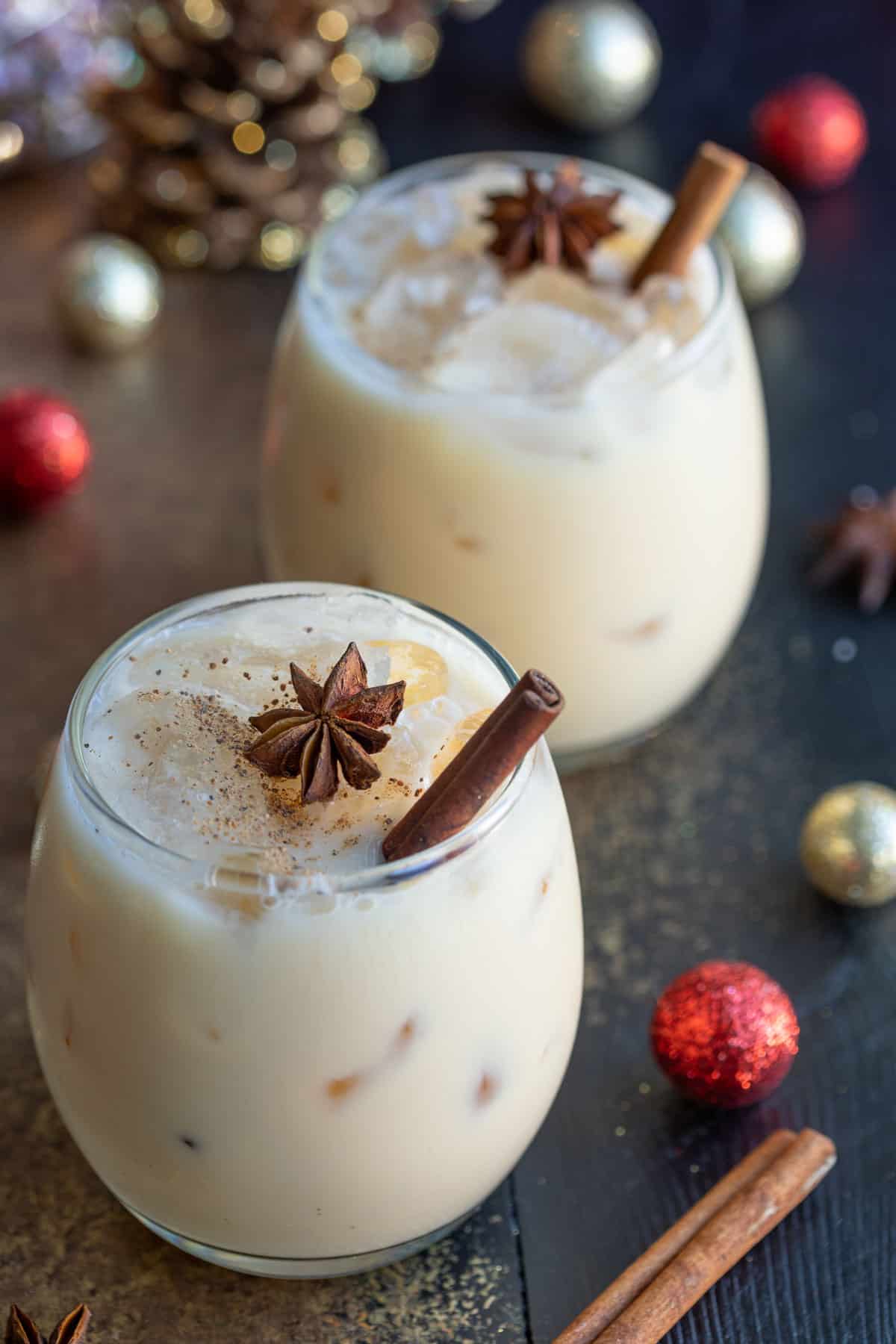 Angled view of two eggnog white Russian cocktails garnished with ground nutmeg, star anise, and a cinnamon stick.