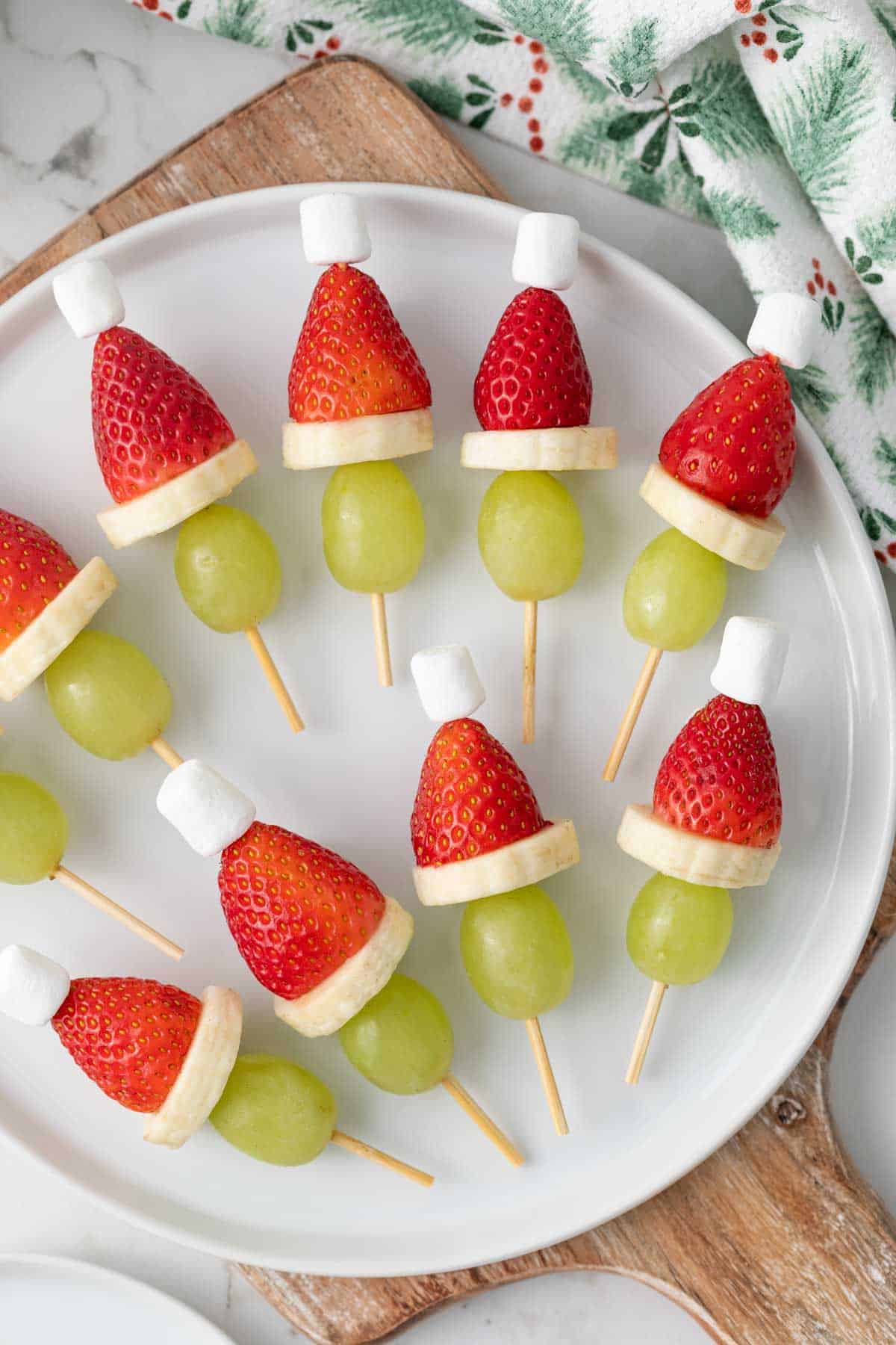 Grinch kabobs with strawberries, grapes, banana slices, and marshmallows on a skewer on a white plate.