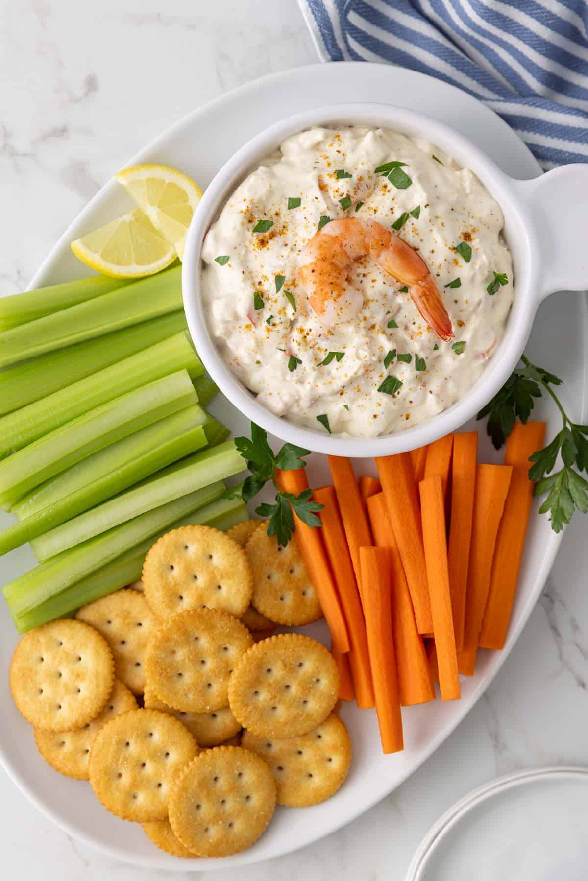 Overhead view of a bowl of shrimp dip on a platter with crackers, celery, and carrots.