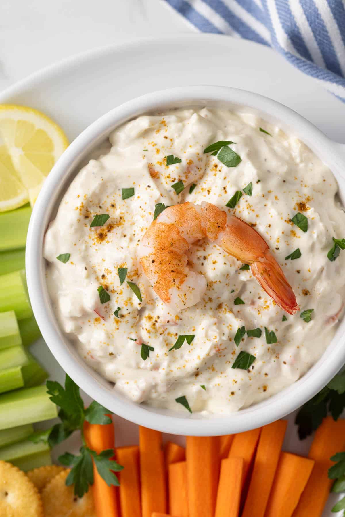 Overhead close up view of a bowl of shrimp dip on a platter with carrots, crackers, and celery.