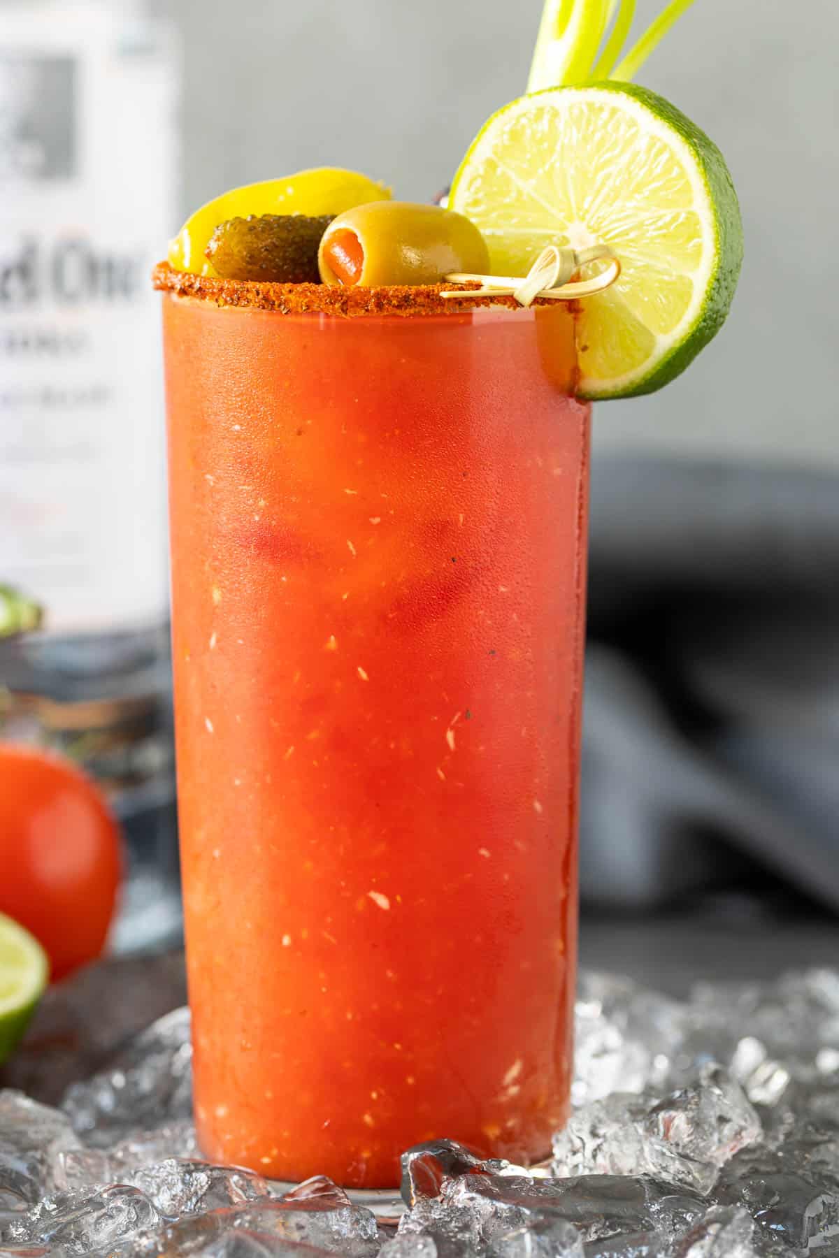 Front view of a bloody mary cocktail. A bottle of vodka is in the background.