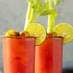 Front view of two bloody mary cocktails. Overlay text is at the top of the image.