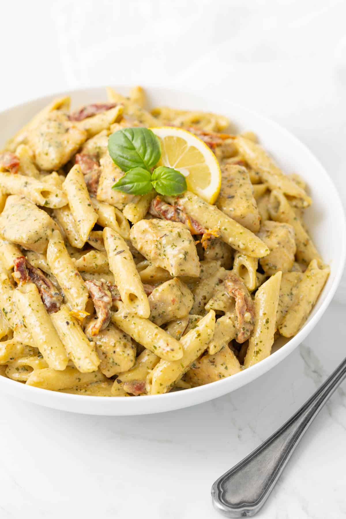 Front angled view of creamy chicken pesto pasta in a white bowl.