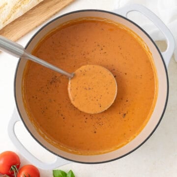 A ladle in a pot of creamy tomato basil soup.
