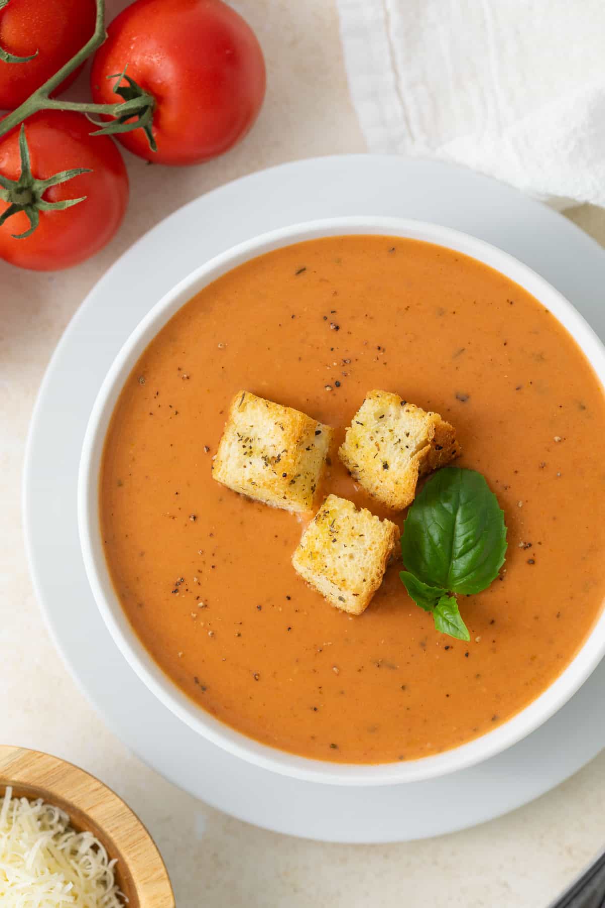 A bowl of creamy tomato basil soup topped with croutons and a fresh basil leaf.