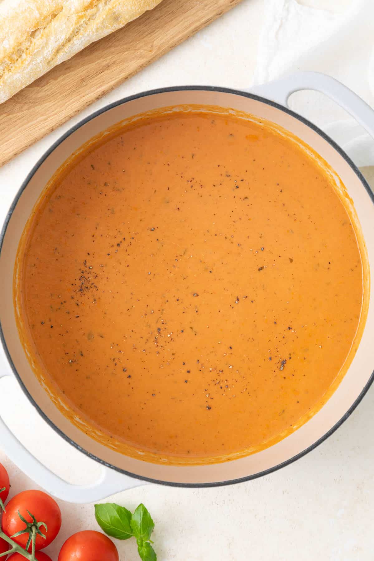 Overhead view of creamy tomato basil soup in a white Dutch oven.