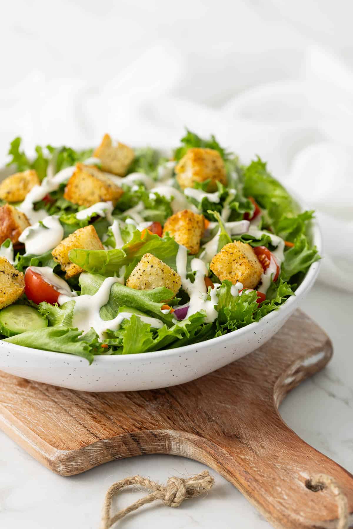 Front view of a garden salad topped with ranch dressing and croutons.