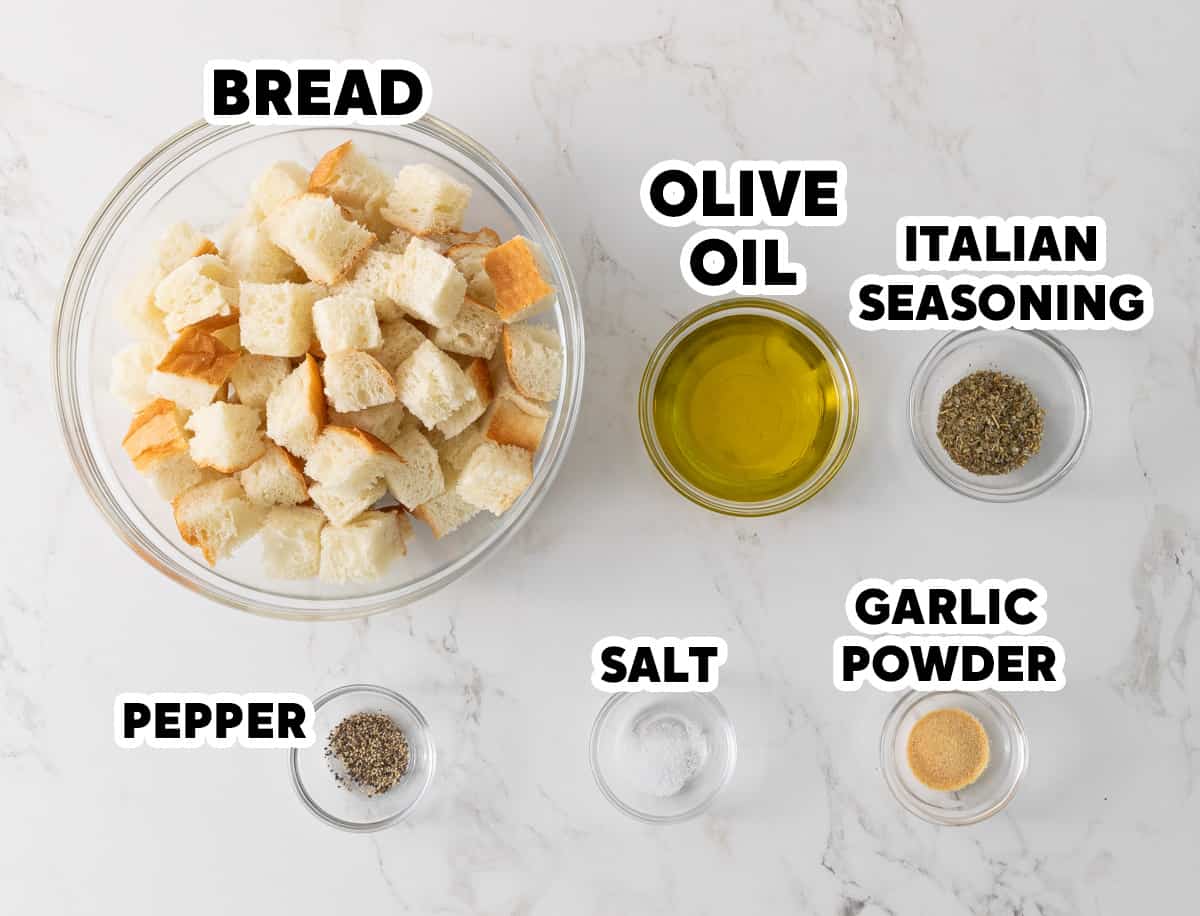 A bowl of cubed bread, olive oil, Italian seasoning, black pepper, salt, and garlic powder.